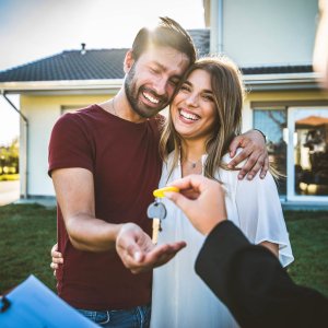 Happy millennial couple receiving keys from realtor, purchasing real estate - Family meeting with real estate agent - New house and real estate concept